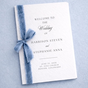 Może przedstawiać: Biały program ślubny związany jasnoniebieską wstążką. Program głosi "WELCOME TO THE Wedding OF HARRISON STEVEN and STEPHANIE ANNA" z datą 23 czerwca 2026 i lokalizacją.