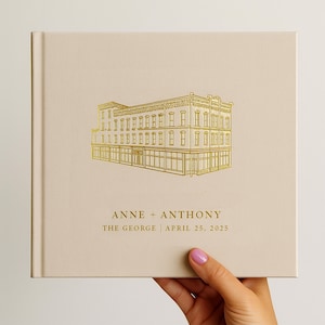 May include: A beige square book with a gold illustration of a building on the cover. The text "ANNE + ANTHONY" and "THE GEORGE | APRIL 25, 2025" are printed in gold below the building illustration.