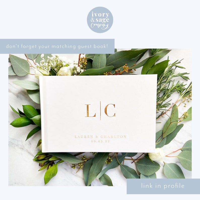 May include: A white guest book with gold lettering, featuring the initials "LC" and the names "LAUREN & CHARLTON" with the date "09.05.22". The book is surrounded by greenery and white flowers. The text "don't forget your matching guest book!" is visible.