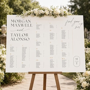 Puede incluir: Un gran cartel blanco de distribución de asientos de boda sobre un caballete de madera, con los nombres Morgan Maxwell y Taylor Alonso, el texto find your seat y una lista de nombres de invitados organizados por letras, con flores blancas.
