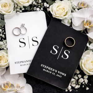 May include: A wedding scene with two vow books, one white and one black, with the initials "S/S". The white book has two diamond rings, and the black book has a gold wedding band. White roses and orchids surround the books.