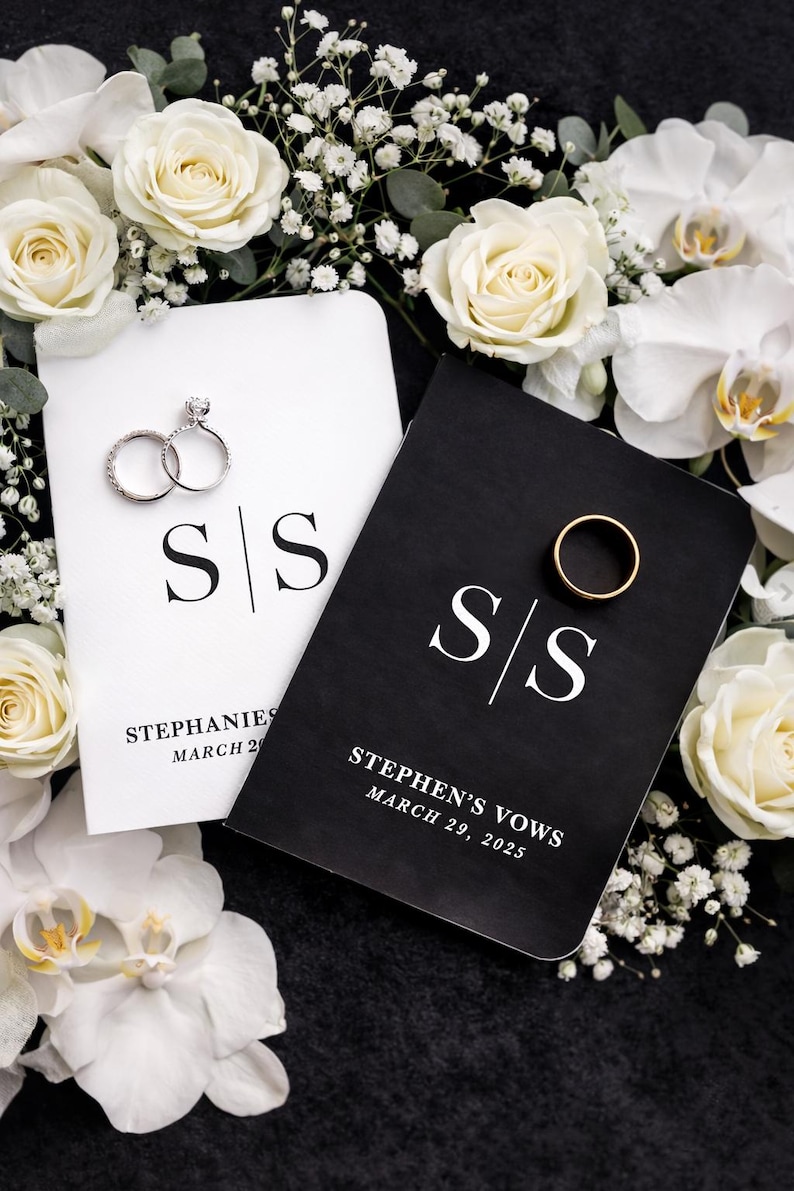 May include: A wedding scene with two vow books, one white and one black, with the initials "S/S". The white book has two diamond rings, and the black book has a gold wedding band. White roses and orchids surround the books.