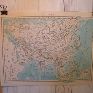 Puede incluir: Un mapa vintage de Asia titulado "Asia Fisica" con un fondo azul claro y líneas marrones que representan las características geográficas. El mapa incluye texto en español, incluyendo los nombres de los países y las regiones.