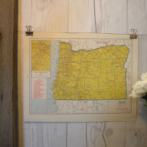 Könnte beinhalten: Eine Vintage-Karte von Oregon, gedruckt auf Papier und mit Clips gerahmt. Die Karte ist gelb und blau mit rotem Text. Die Karte zeigt die Countys des Bundesstaates und die wichtigsten Städte.