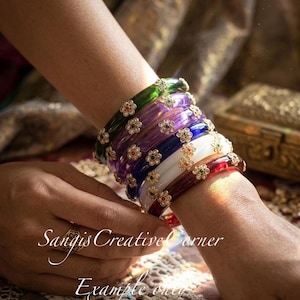 May include: A collection of colorful bangles in shades of green, purple, blue, white, and red. Each bangle is adorned with small, flower-shaped embellishments. The text "Sangis Creative Corner Example only" is visible.