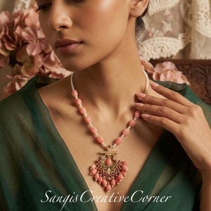 May include: A necklace featuring peach-colored ribbed beads and small white pearls, centered by a gold-toned pendant with pink and green stones and hanging bead accents. The text Sangis CreativeCorner is visible at the bottom of the image.