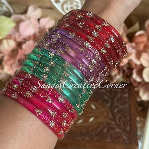 May include: A collection of vibrant bangles in red, pink, green, and purple hues. Each bangle is decorated with tiny, glittering details. The text "Sangus Creative Corner" is displayed on the bangles.