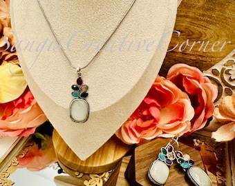 May include: A silver necklace and earrings set with a white stone pendant and matching earrings. The pendant and earrings are decorated with colorful stones.