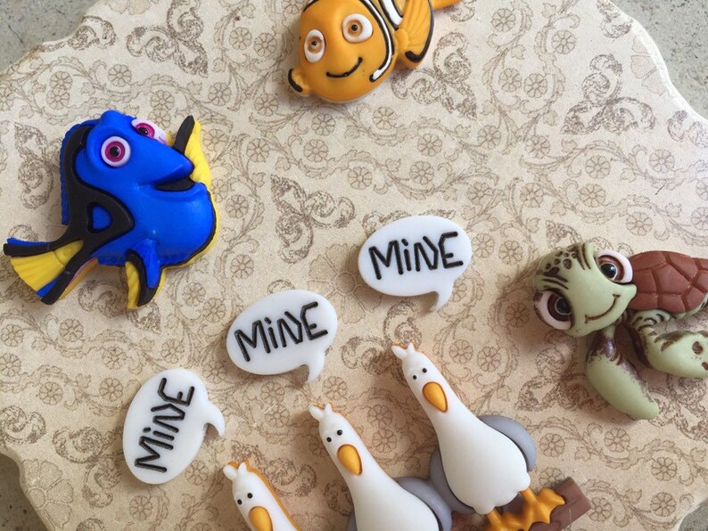 May include: A collection of colorful resin character embellishments featuring characters from the movie "Finding Nemo". Includes Dory, Nemo, a sea turtle, and seagulls. Several speech bubbles say "MINE".