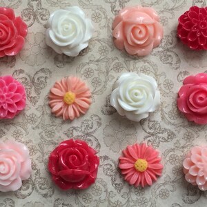 May include: Twelve assorted resin flower embellishments in shades of pink, white, and red. The flowers are in various styles, including roses, daisies, and carnations.