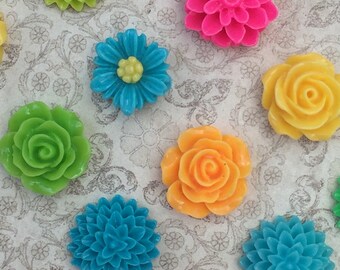 Op de afbeelding: Assortiment van kleurrijke plastic bloemenversieringen in verschillende vormen en maten. De bloemen zijn in tinten groen, blauw, roze, geel en oranje.
