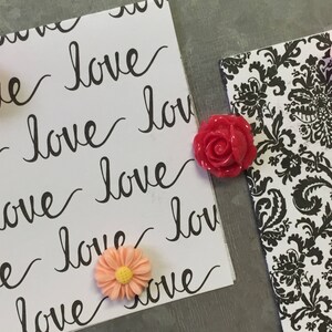 May include: Two white cards with the word "love" written on them in black cursive. The cards are decorated with pink and red flower-shaped push pins.