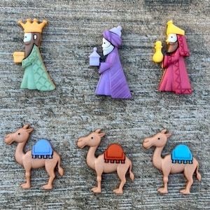 May include: Set of six Christmas ornaments featuring the three wise men and their camels. The wise men are wearing colourful robes and crowns, and the camels are brown with colourful saddles.