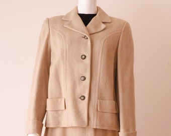 May include: A beige wool suit jacket and skirt set. The jacket has a notched collar, four button closure, and flap pockets. The skirt is knee-length.