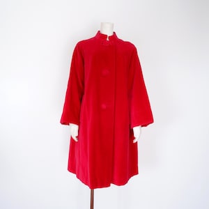 May include: A vibrant red coat featuring a high collar, long sleeves, and a front button closure with three large, matching red circular buttons. The coat has a straight, loose silhouette that falls below the hips, providing a clean, structured look.