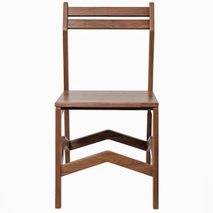 May include: A wooden chair with a minimalist design. The chair features a rectangular seat, a backrest with two horizontal slats, and angled legs joined by a chevron-shaped support. The wood has a warm, natural tone.