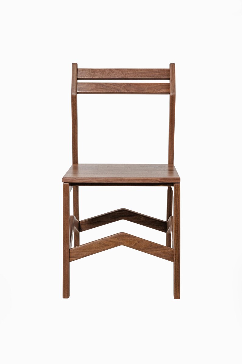 May include: A wooden chair with a minimalist design. The chair features a rectangular seat, a backrest with two horizontal slats, and angled legs joined by a chevron-shaped support. The wood has a warm, natural tone.