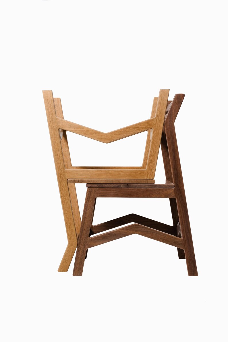 May include: Two wooden chairs, one light-colored and one dark-colored, are stacked against each other. The chairs have a modern design with geometric shapes and angled legs. The light-colored chair is in front, and the dark-colored chair is behind.