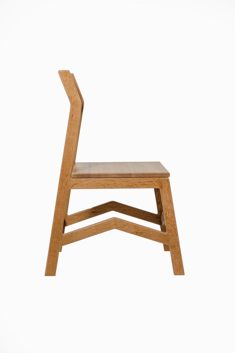 May include: A side view of a wooden chair with a light brown finish. The chair has a straight back with a curved top, a rectangular seat, and a geometric base. The chair's dimensions are approximately 36 inches high, 18 inches wide, and 18 inches deep.
