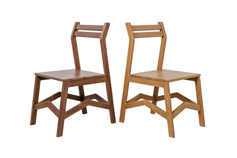 May include: Two wooden chairs with a minimalist design. One chair is a dark brown, the other is a light brown. Both chairs have a square seat, angled legs, and a back with two horizontal slats.