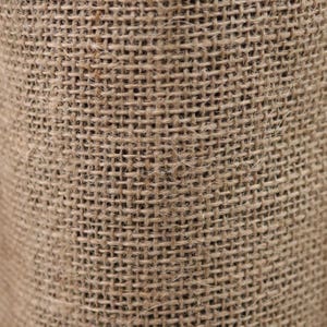 May include: A close-up view of a coarse, tan-colored burlap fabric featuring a distinct, open-weave grid pattern. The material displays a natural, fibrous texture with visible individual strands of jute woven together in a simple, uniform crisscross design.
