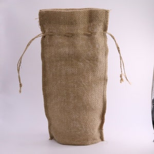May include: A tall, rectangular drawstring bag crafted from natural tan-colored burlap fabric. The bag features a coarse, woven texture and includes two thin, matching jute strings threaded through the top hem for closure and carrying purposes.