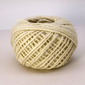 May include: A ball of natural-colored twine, tightly wound into a compact sphere. The twine appears to be made of a fibrous material, with a slightly textured surface. The overall color is a soft, creamy beige. Ideal for crafting and packaging.