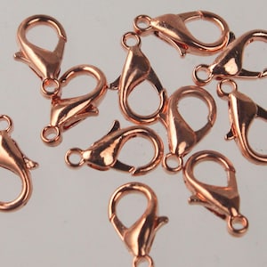 May include: A collection of rose gold-colored lobster claw clasps. These clasps are designed for jewelry making and feature a spring-loaded mechanism for secure closure. The clasps are made of metal and have a shiny finish. They are scattered across a light background.