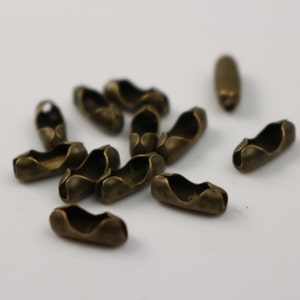 May include: Close-up of several antique brass-colored chain connectors. The connectors are oval-shaped with a curved design and two openings on each end. They are scattered on a white surface, suggesting a craft or jewelry-making theme.