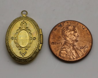 May include: A gold-toned oval locket with an ornate design. The locket is about the size of a US penny.