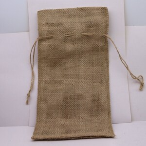 May include: A rectangular drawstring pouch crafted from tan-colored, coarse-woven burlap fabric. The bag features a simple top closure mechanism with two thin, matching jute strings extending from the sides, allowing for easy opening and closing.