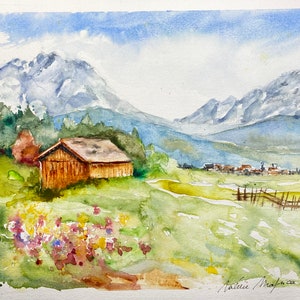 Puede incluir: Pintura acuarela de una cabaña de madera en un campo verde con un pequeño pueblo en la distancia y montañas cubiertas de nieve en el fondo.