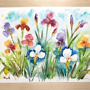 Può includere: Un dipinto ad acquerello su carta che raffigura una vivace scena di giardino con vari fiori di iris nelle tonalità del viola, giallo, bianco e rosa, su uno sfondo blu tenue con fogliame verde e una firma nell'angolo in basso a destra.