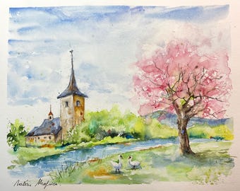 Sensación de primavera, pintura de acuarela original de un paisaje rural primaveral, árbol rosa y pequeño pueblo junto al agua tranquila.