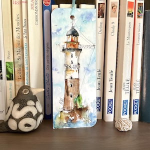 Op de afbeelding: Een rechthoekige boekenlegger met een aquarelillustratie van de Men-Ar vuurtoren. De vuurtoren is geschilderd in bruin-, wit- en grijstinten tegen een lichtblauwe lucht met kleine vogels. Aan de bovenkant is een lichtblauw lint bevestigd.
