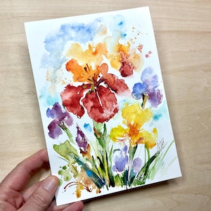 Può includere: Dipinto ad acquerello di fiori di iris colorati nelle tonalità del rosso, arancione, giallo e viola. L'opera d'arte presenta uno stile sciolto ed espressivo con pennellate visibili e schizzi di acquerello. Steli e foglie verdi completano la composizione floreale.