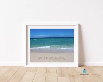 May include: A framed photograph of a beach scene with the word "DREAM" written in the sand. The ocean is a bright turquoise blue and the sky is a clear blue with white clouds.
