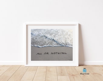 May include: A white framed print with a photograph of a beach scene. The ocean waves are crashing on the shore, and the words "All or Nothing" are written in the sand.