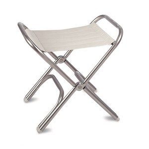 Peut inclure: Un tabouret pliant argenté avec un siège en tissu beige. Le tabouret a une poignée au dos et une base en forme de croix.
