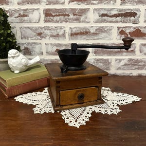 Molinillo de café antiguo de madera primitiva con tapa de hierro fundido y manivela de madera. Decoración rústica para cocina de estilo campestre.