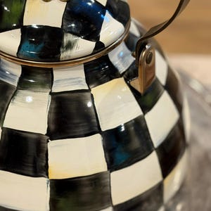 May include: A decorative black and white checkered teapot with a gold rim and handle. The lid features a gold filigree design and a red knob. The teapot is on a silver tray.