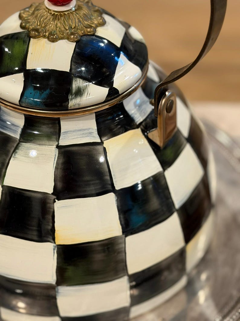 May include: A decorative black and white checkered teapot with a gold rim and handle. The lid features a gold filigree design and a red knob. The teapot is on a silver tray.