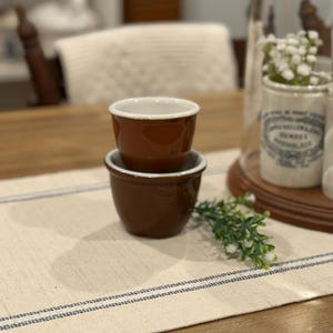 May include: A white ceramic mug with a black handle and the text "But First, Coffee" in a bold, black font. The mug is set against a blurred background, suggesting a cosy setting.