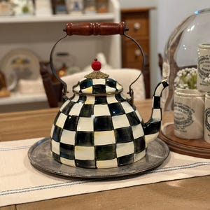 May include: A decorative black and white checkered teapot with a wooden handle and a red knob on top. The teapot sits on a silver tray, showcasing a classic design. The teapot is a kitchenware item.