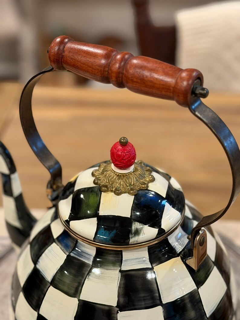 May include: A decorative tea kettle with a black and white checkered pattern. The handle is made of dark wood, and the lid features a red, ornate finial. The kettle's handle is made of dark metal.