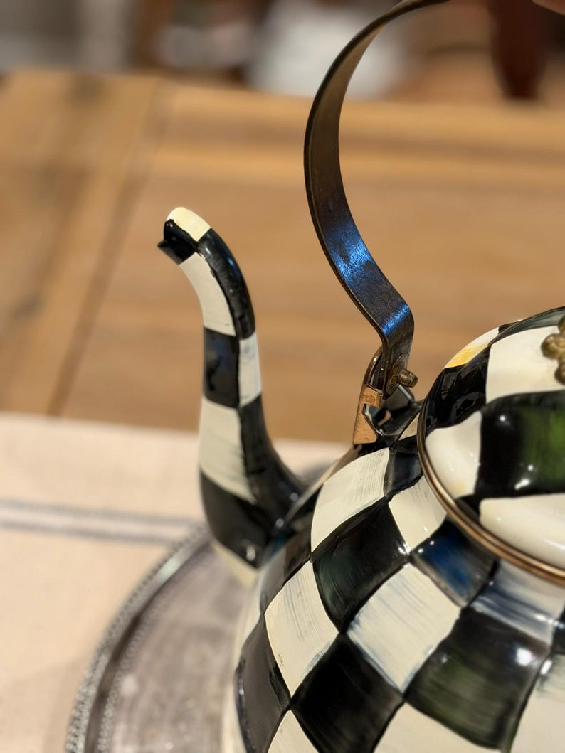 May include: A decorative black and white checkered teapot with a curved handle and spout. The teapot has a gold-colored rim and handle attachments. The spout is black and white striped.