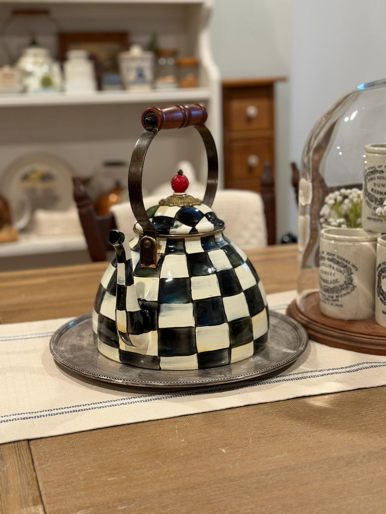 May include: A decorative black and white checkered teapot with a wooden handle and a red cherry-shaped finial. The teapot sits on a silver tray, suggesting a kitchen or dining setting.