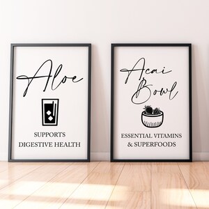 May include: Two black framed prints with white backgrounds. The left print features a black illustration of a glass of aloe juice and the text "Aloe" and "Supports Digestive Health". The right print features a black illustration of a bowl of acai with the text "Acai Bowl" and "Essential Vitamins & Superfoods".