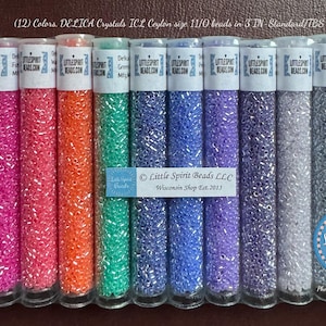 Può includere: Dodici tubetti di perline Delica Crystal Ice Ceylon di misura 11/0 in vari colori, tra cui rosa, arancio, verde, blu, viola e nero. I tubetti sono etichettati con il nome dell'azienda "Little Spirit Beads LLC" e l'indirizzo del sito web "littlespiritbeads.com".