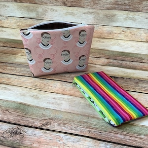 May include: Two zippered pouches, one pink with a repeated pattern of a woman's face and the symbol for female, the other a rainbow striped pattern.